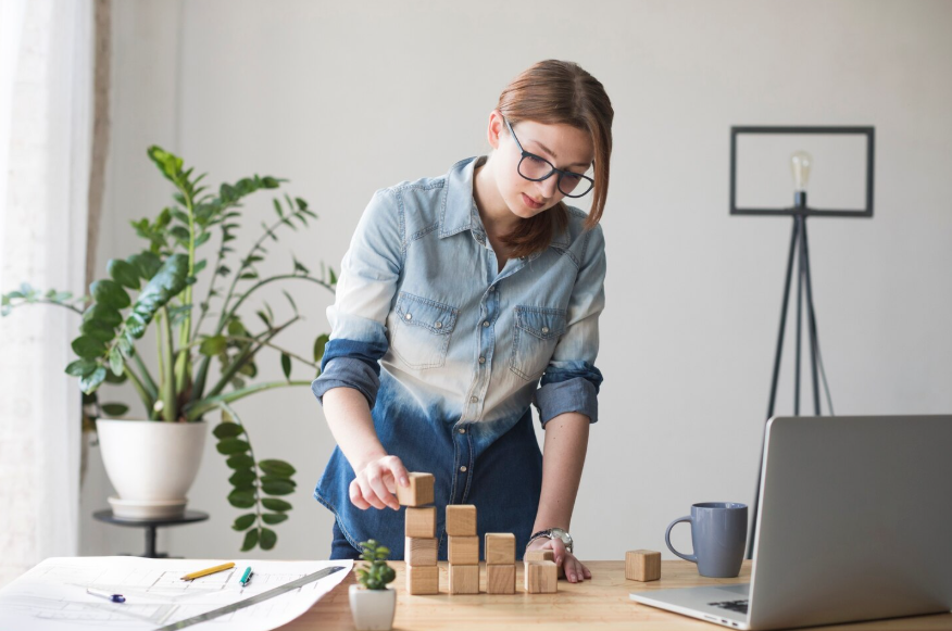 Woman stacking wooden blocks, illustrating small changes producing big results through gradual progress