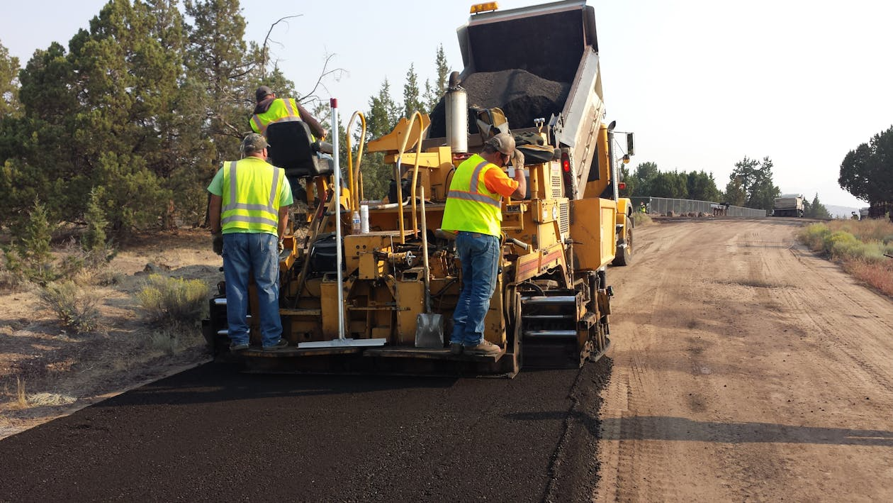 Road construction crew laying asphalt, illustrating road lifespan factors like pavement materials and foundation quality.