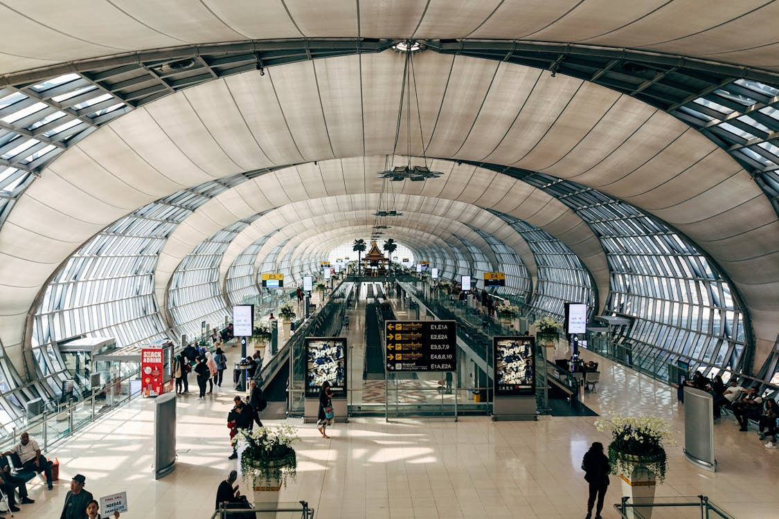 Wide airport terminal with signs and travelers, illustrating airport layout design and passenger flow.